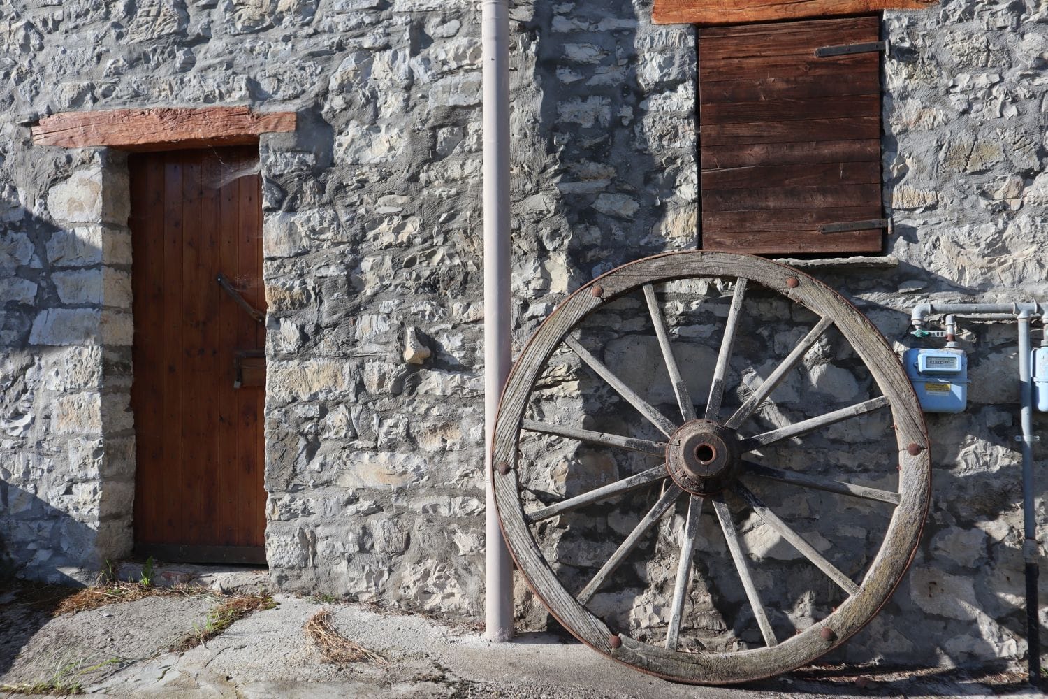 Una vecchia ruota di carro in legno appoggiata al muro di pietra di un borgo